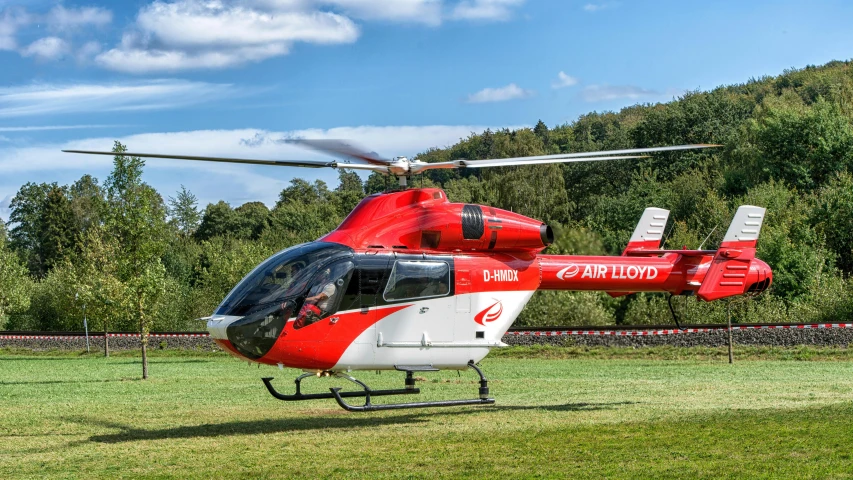 a red and white helicopter on grass near trees