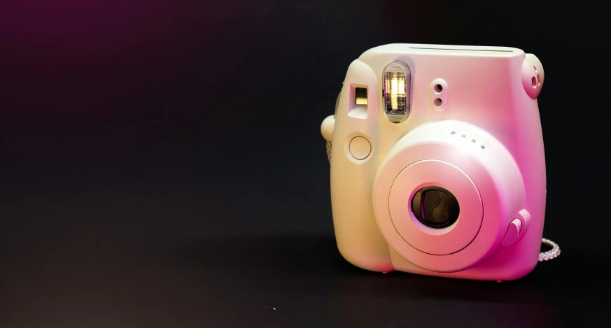 a pink camera that is sitting up against a purple background