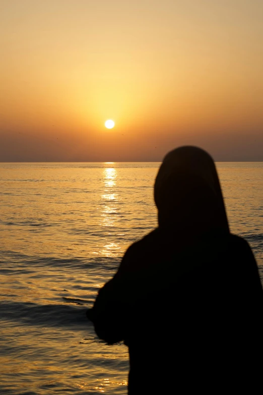 someone standing at the ocean with a sunset behind them