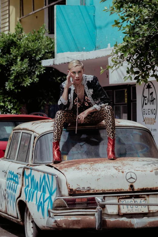 a woman sits on top of an old rusted out car in a dirty street