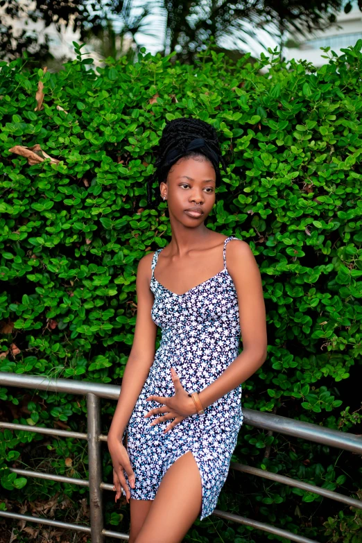 a woman poses in front of a bush and railing