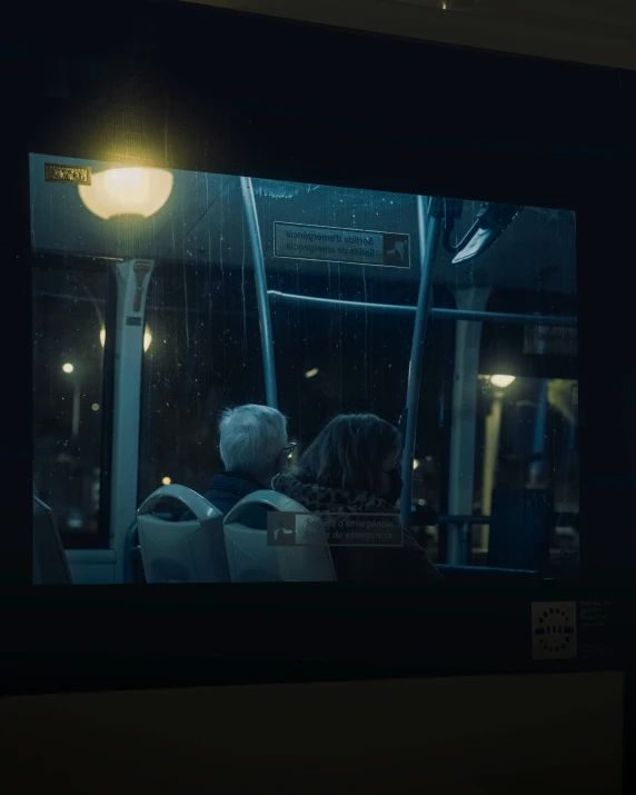 an old man and woman sit in the dark on a bus