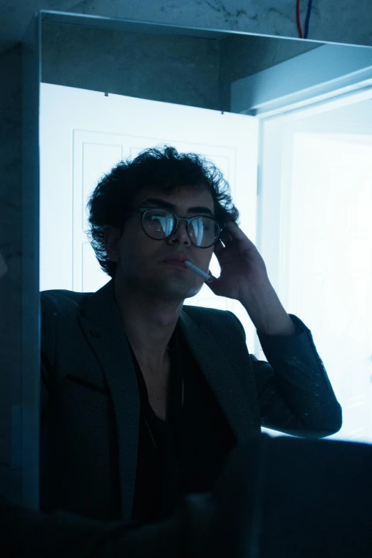 a man in glasses talking on the phone while sitting in a chair