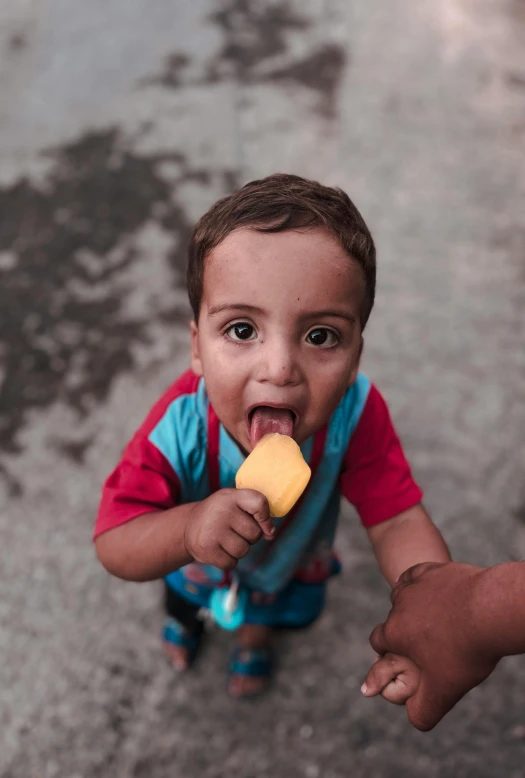 a child eating an ice cream treat, his hands on his hip