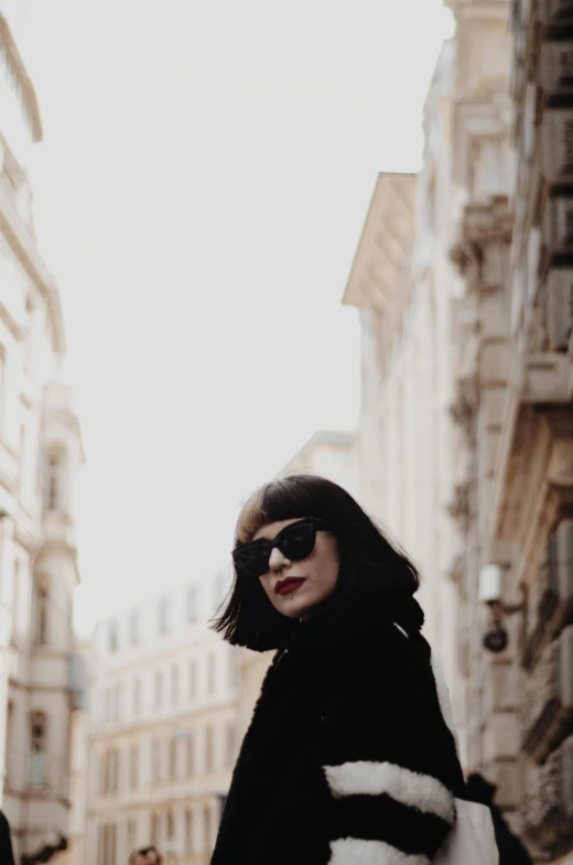 a woman in black fur coat standing on street next to buildings