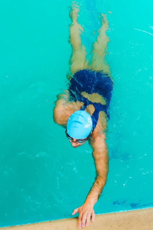 a man dives in an aqua pool while wearing a hat