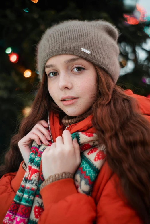 a girl wearing a hat and scarf is standing in front of a christmas tree