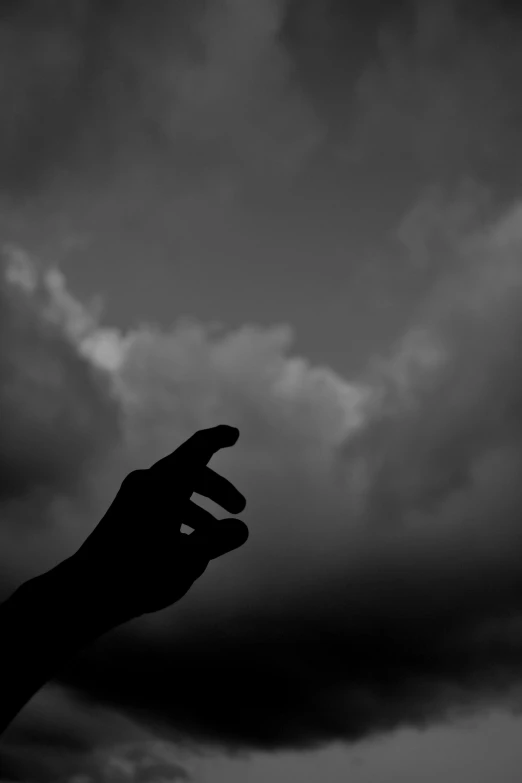 a black and white po of someone's hand reaching towards a storm cloud