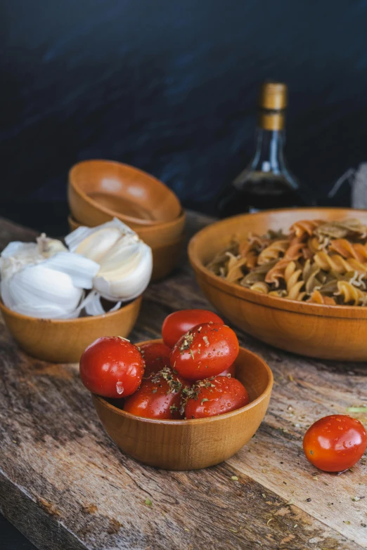 some noodles in bowls on a wood table with garlic and tomatoes