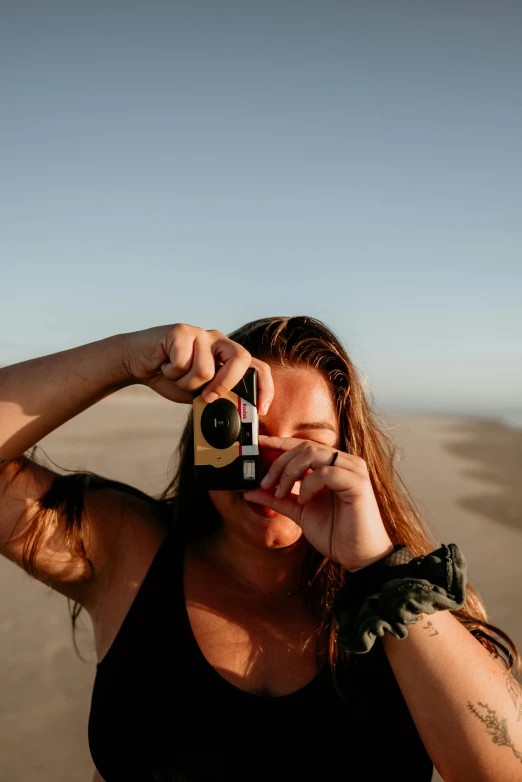 a girl takes a picture with her camera while standing on the beach