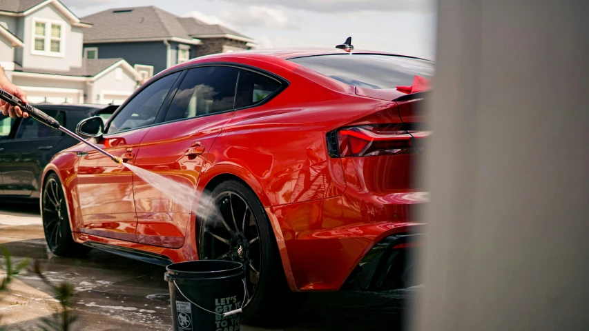 a red car being washed by a man with a high pressure washer