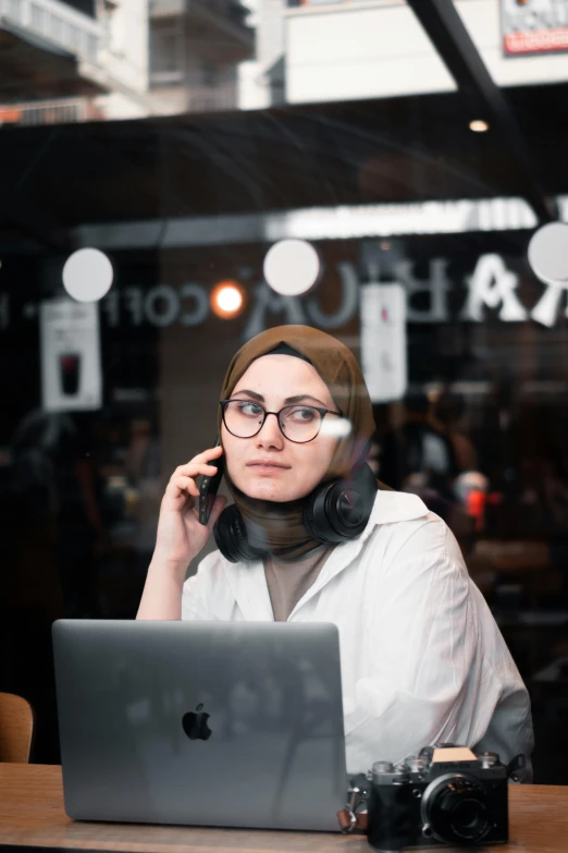 a woman sitting at a table with a laptop and cell phone in her hand