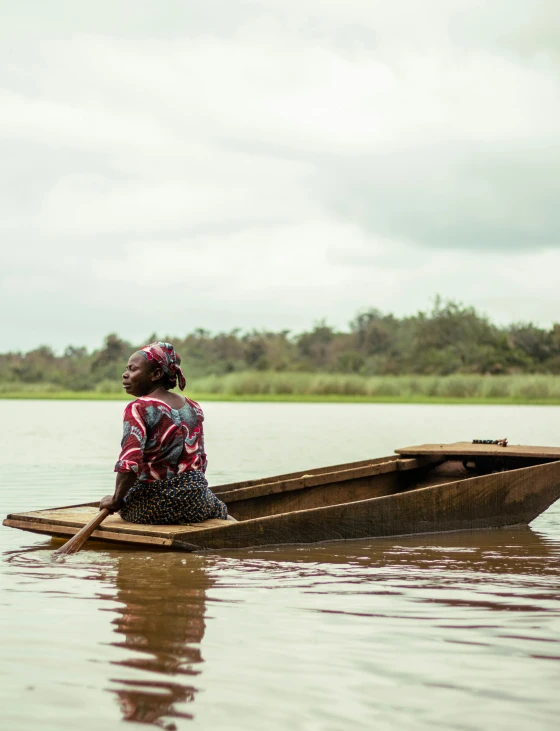 a woman sitting on top of a wooden boat in a lake