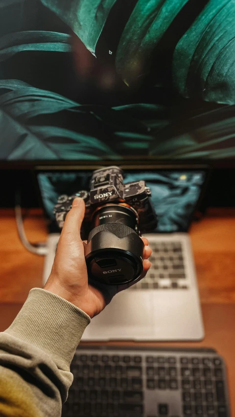 a person holding a camera while in front of a laptop