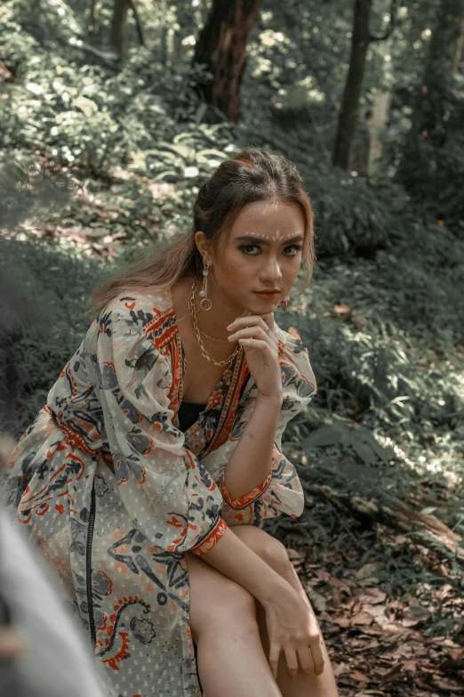 a woman sitting in the forest holding her finger up