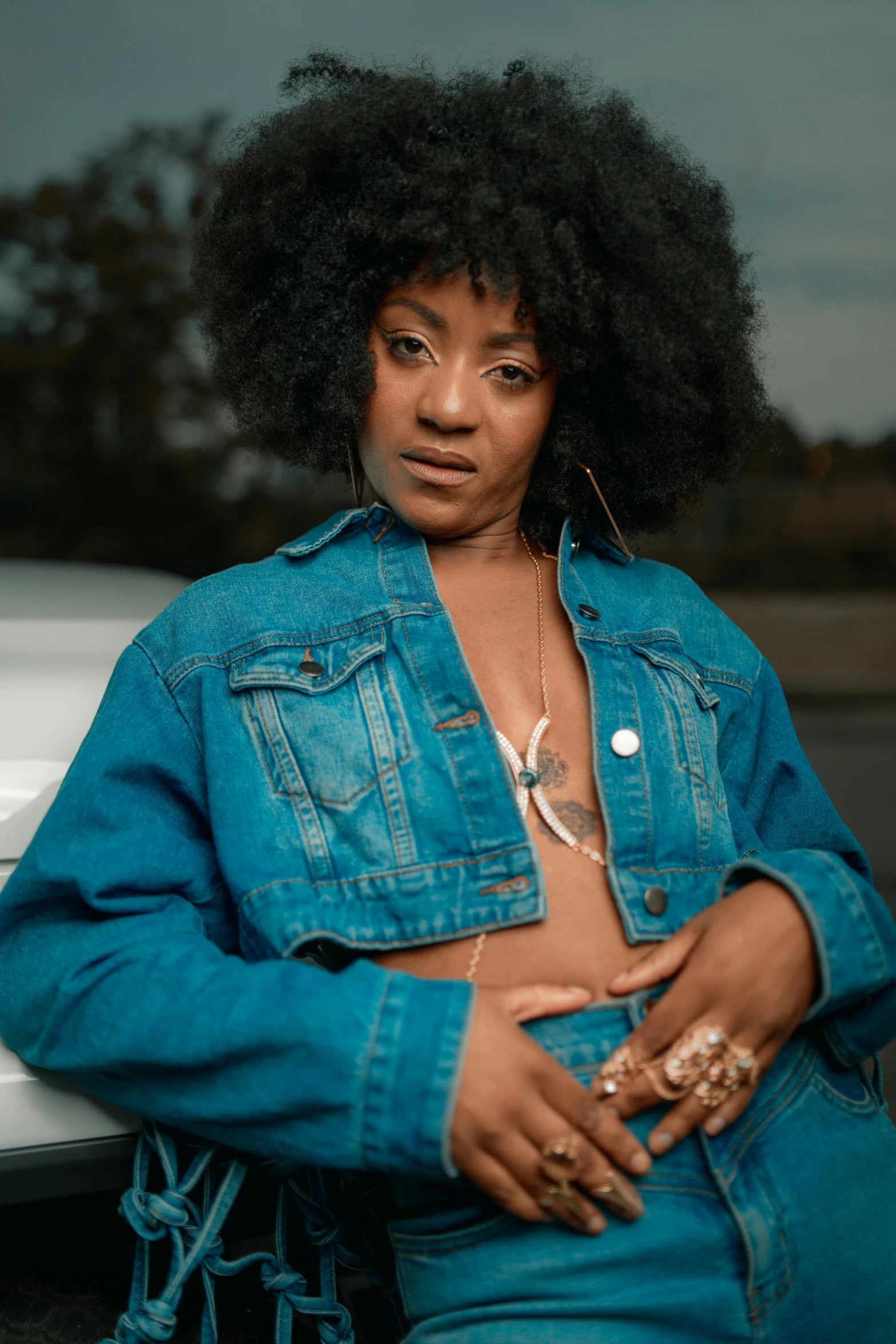 a woman in denim clothes is sitting next to a white car