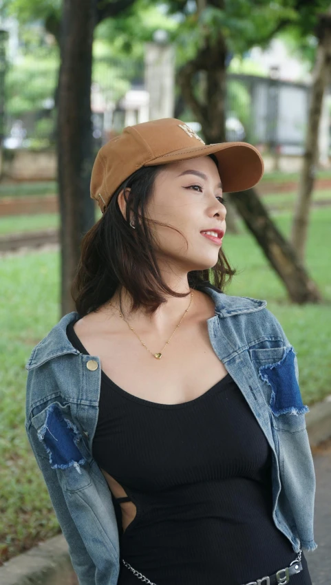 a woman is standing on a sidewalk in a jean jacket and hat