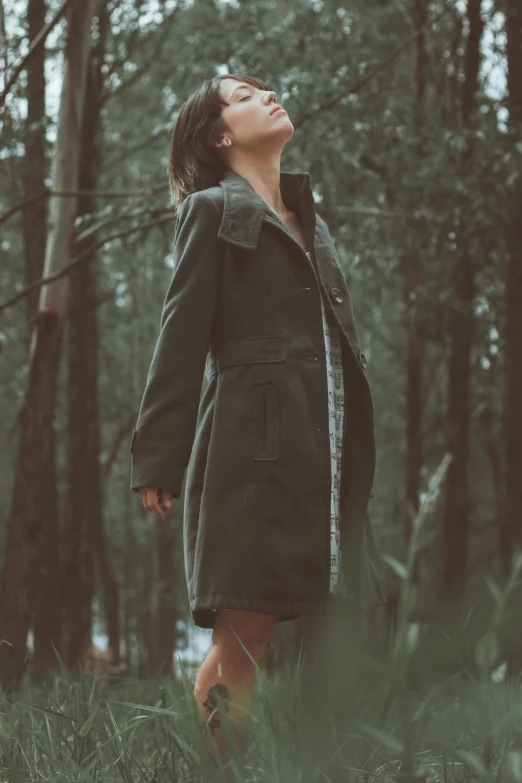 a woman in a coat looking upward in the woods