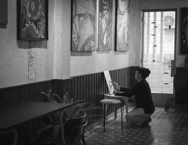 a woman sits in a dark room while holding a piece of art