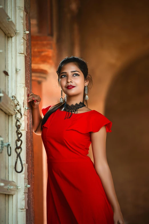 an attractive young lady in a red dress leaning against a wall