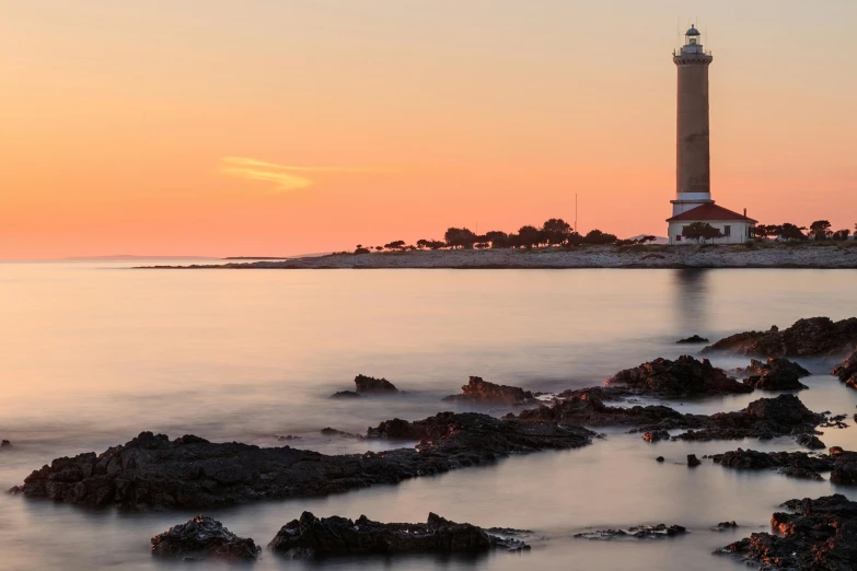 the sun is setting behind the water at a lighthouse