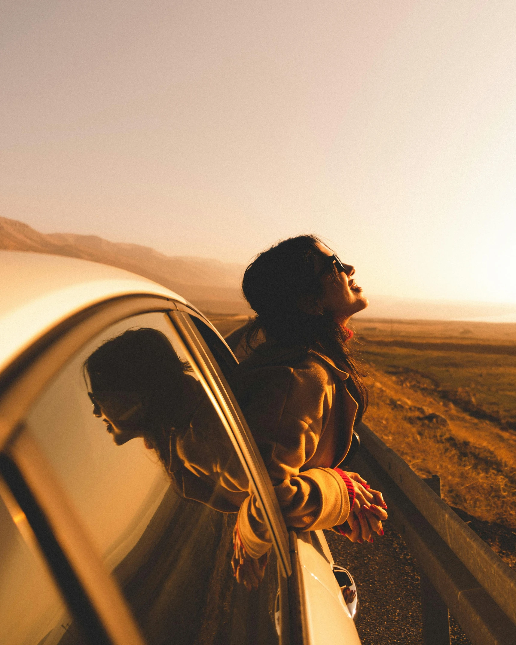 a man with long hair standing by a car in the desert