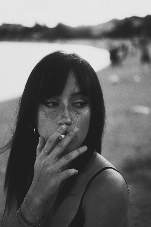 a young woman smokes a cigarette in front of the ocean