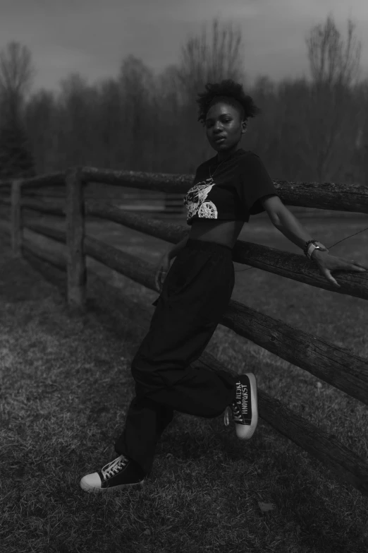 woman in a black outfit leaning on a wooden fence