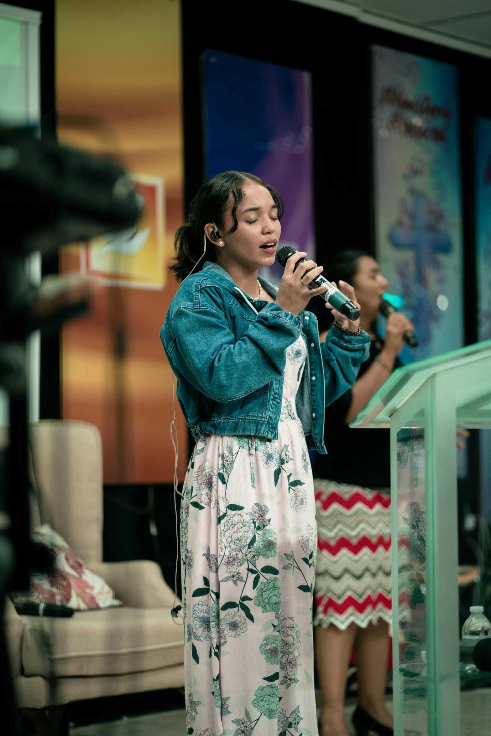 a woman in a floral print dress holds a microphone and sings