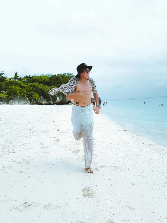 a man walking on the beach while wearing a shirt