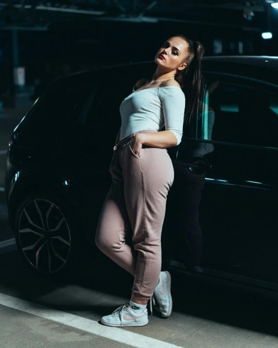 a young woman leaning on the front door of a black car