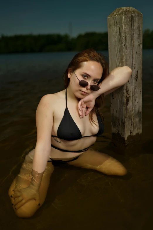 the girl is wearing a black bikini posing in muddy water