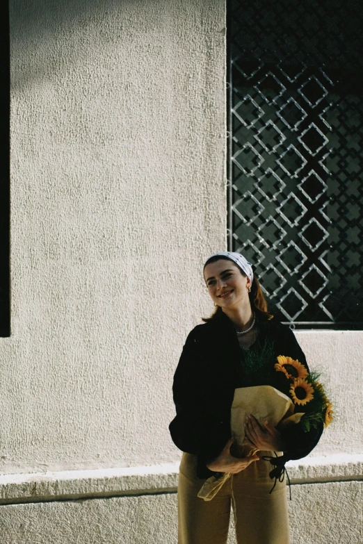 a smiling woman holding sunflowers standing in front of a building