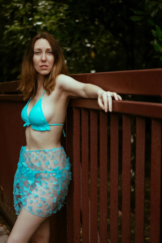 a woman poses on a bridge in a blue bikini