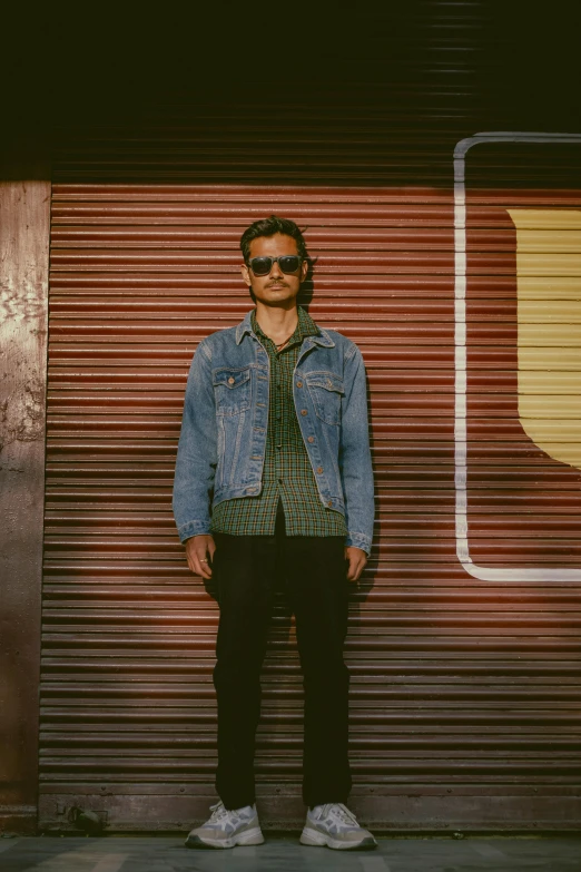 a man standing against a corrugated metal wall with sunglasses on