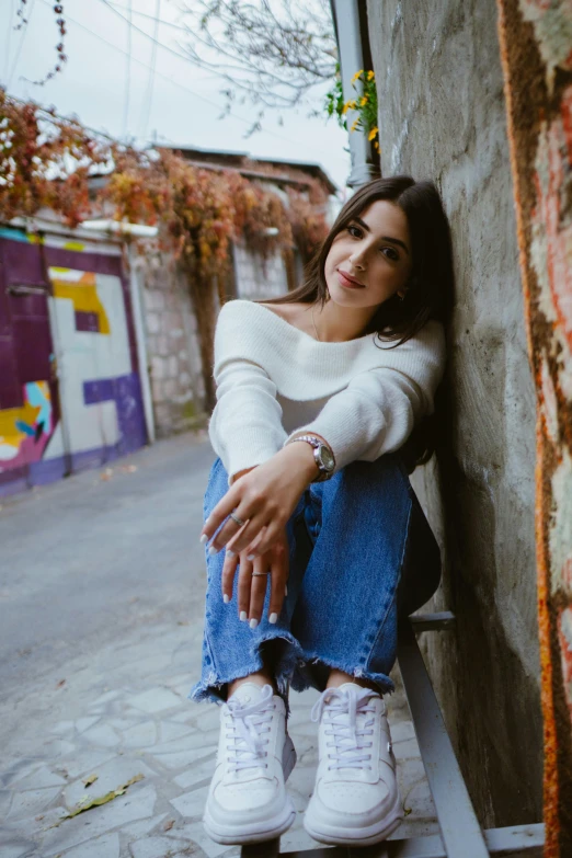 a beautiful young woman sitting on a bench near a building