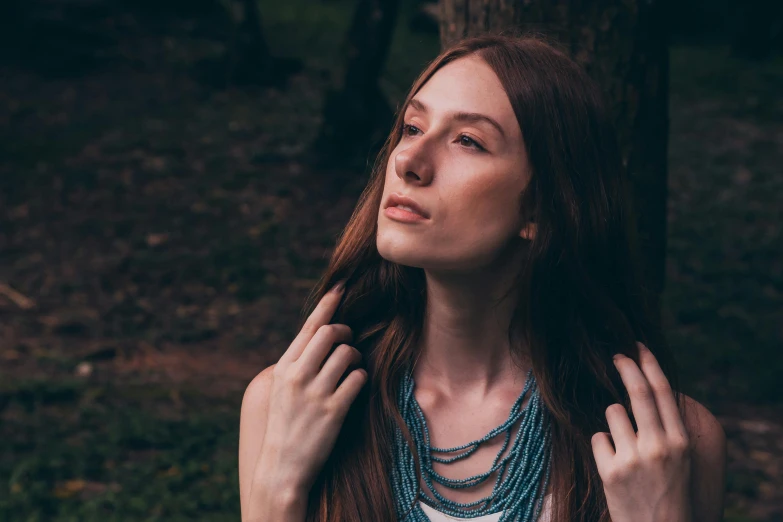 a woman in blue beads and a white shirt holding her hair