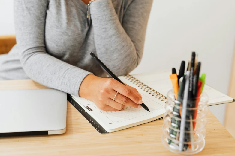 a lady with her hand on her pen sitting at a table with notebook and pens