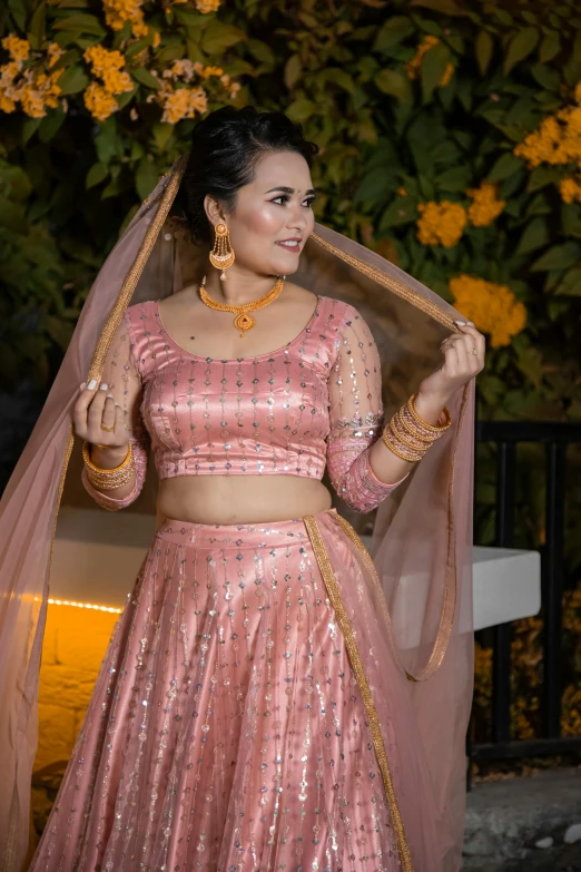 a woman with dark hair wears a pink dress, veil and jewelry