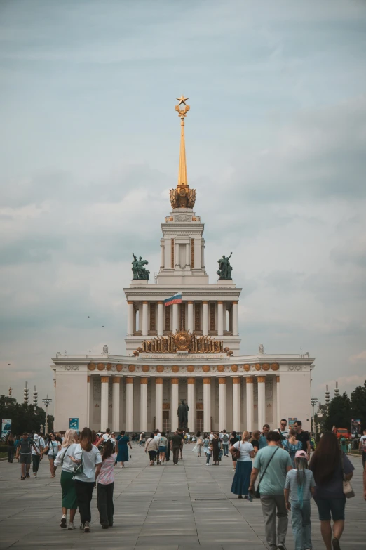 a group of people walking toward a building that has columns with gold statues