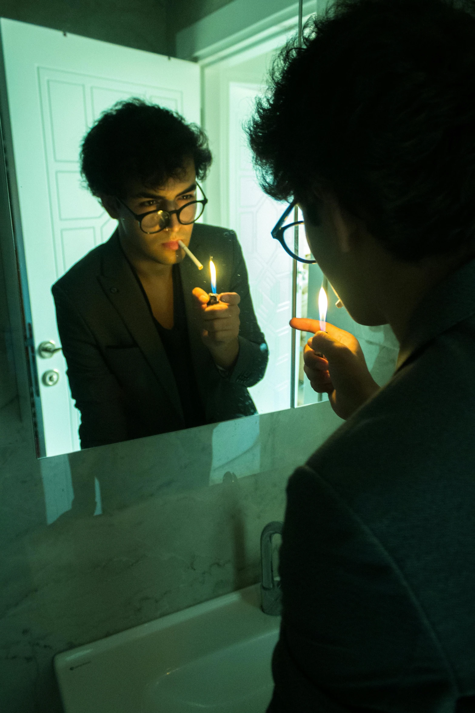 a man with glasses, dark hair and glasses on is brushing his teeth with his hand and a lit candle is in front of him