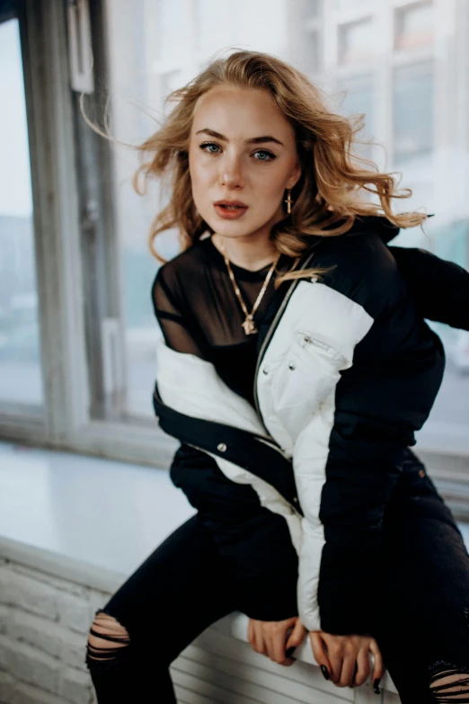 young woman leaning on ledge in a black and white jacket