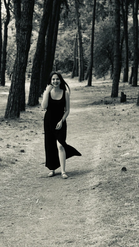 a woman in a black dress walks through a forest