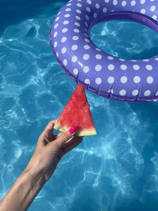 someone is holding a slice of watermelon in a pool