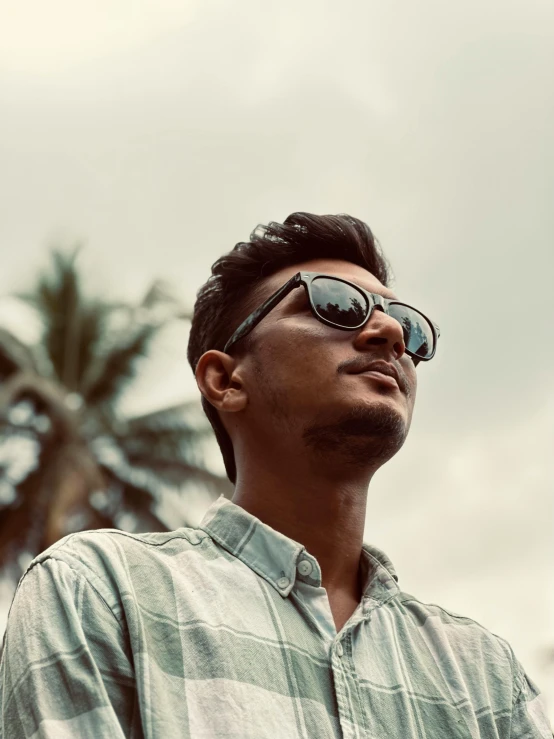 a man standing by a palm tree wearing sunglasses