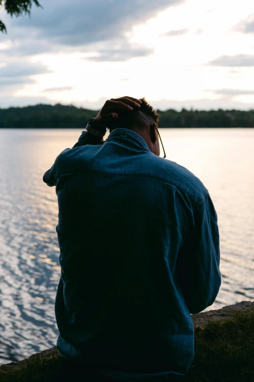 a man sits on the shore of a lake and looks at the water while talking on a cell phone