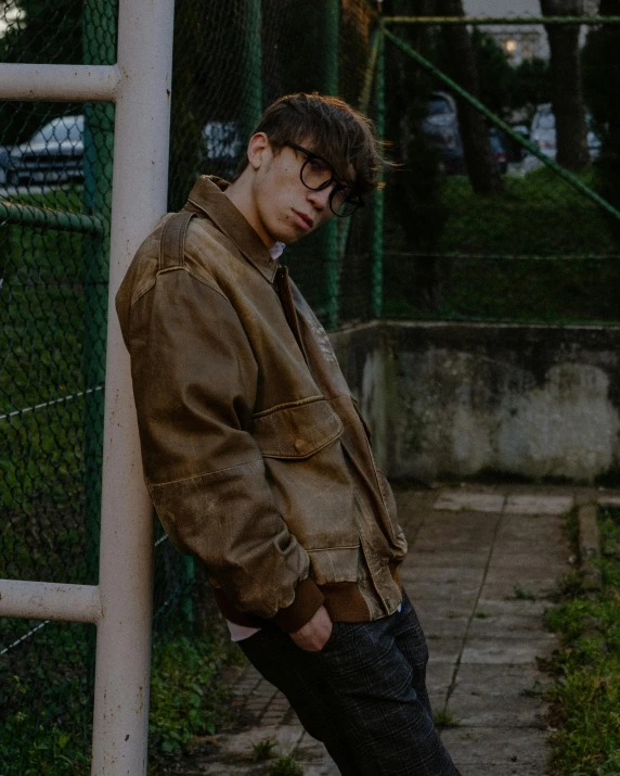 a man in glasses leaning against a fence