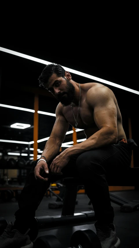 a shirtless man with  on is sitting on a bench in the gym