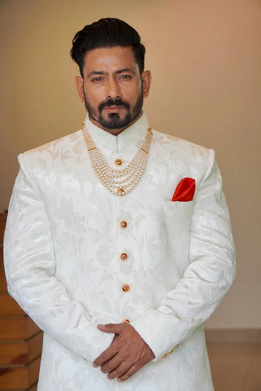 an indian groom wearing a white sherwa suit and red rose