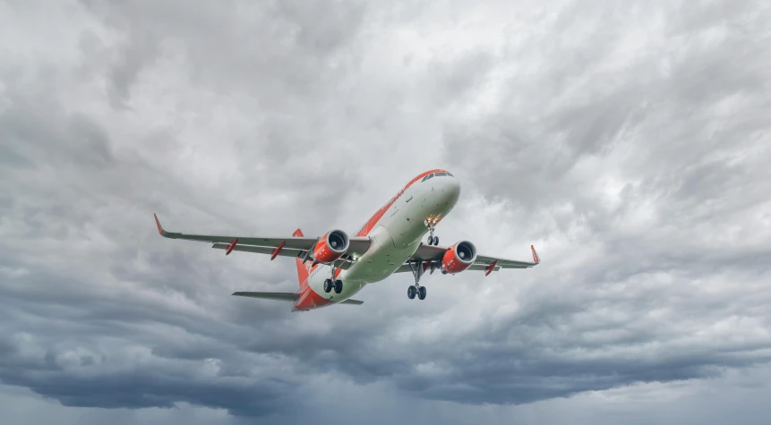 airplane with red and orange trim flying in cloudy sky